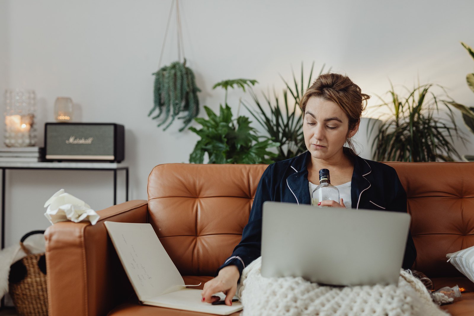 Someone sitting on a sofa in the evening with a notebook open on one knee and a pen in hand.