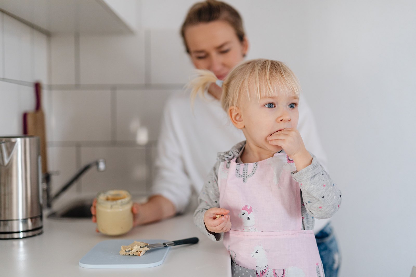 A mechanical kitchen timer on a counter, dial turned to a few minutes, with a child playing in the background.